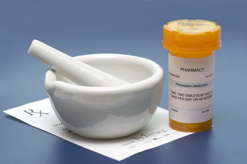 Mortar and pestle, prescription slip, and labeled medicine bottle on a blue pharmacy workbench